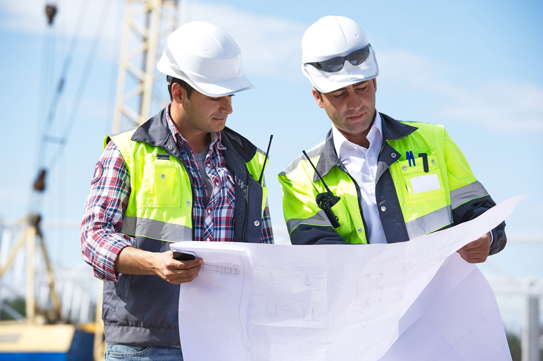 Two engineers at construction site are inspecting works on site according to design drawings.