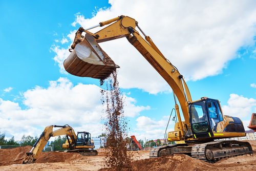 A yellow and black excavator some dirt trees and clouds