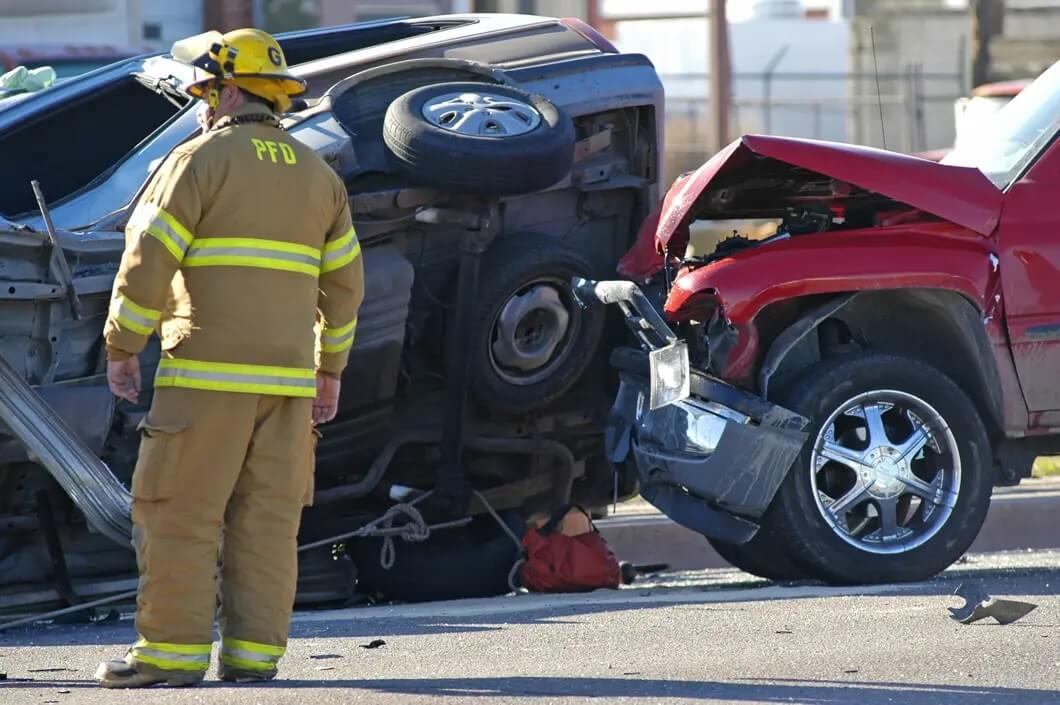 A fireman standing next to an overturned car.